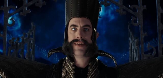 A close-up of Time, a character from the 2016 Disney movie "Alice Through the Looking-Glass." He has a tall, dark hat, a distinctive mustache, and bright blue eyes, and is set against a dark, mysterious background with metallic structures.