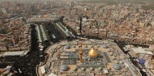 An aerial view of the Arbaeen pilgrimage in Iraq (2018), showing massive crowds gathered around the golden-domed shrine in the city of Karbala. The densely packed pilgrims are seen making their way through the city, paying their respects during one of the largest religious gatherings in the world.