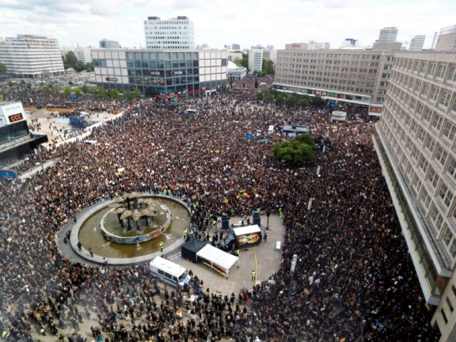 An aerial view of a large crowd gathered at Alexanderplatz in Berlin during a Black Lives Matter protest in 2020. The image captures the demonstration with people holding signs and banners advocating for racial justice and equality.