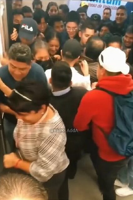 A large crowd of people pushing and shoving to get onto a train, not allowing passengers to exit first. The scene is chaotic, with individuals tightly packed together, demonstrating the intensity of the situation.