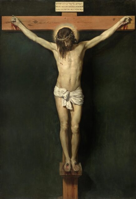 Jesus nailed to the cross, his head bowed forward with his hair partially covering his face. Blood flows from his wounds on his hands, feet, and side, and a faint halo surrounds his head. Above the cross is an inscription in Latin, Greek, and Hebrew, declaring "Jesus of Nazareth, King of the Jews."