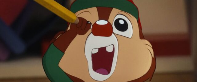 A scene from "Chip 'n Dale: Rescue Rangers" (2022) showing the character Dale pretending to stab himself in the right eye with a pencil. His mouth is wide open in a dramatic expression, emphasizing the playful and exaggerated nature of the moment.