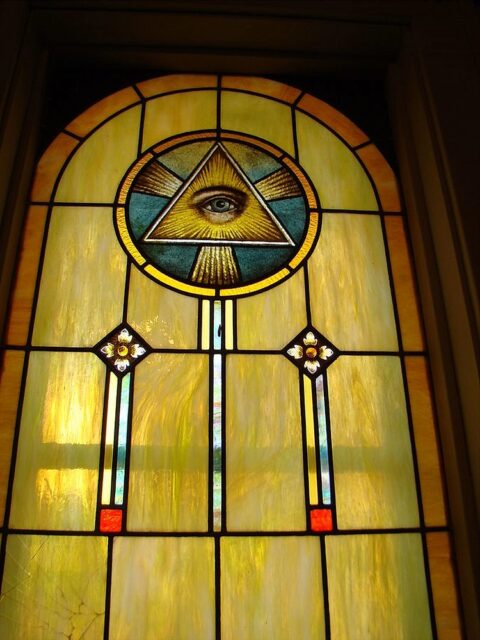 A yellow stained glass window in the St. Francis of Assisi Catholic Church in Fifield, Wisconsin, depicting the Eye of Providence within a triangle, surrounded by rays of light.