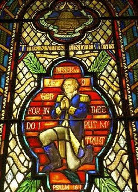 A stained glass window in The White House Chapel in Washington, USA, depicting George Washington kneeling in prayer. Above him, the Eye of Providence is enclosed in a triangle above a pyramid. The text reads, "Preserve me, O God, for in thee do I put my trust" from Psalm 16:1, along with the phrase "This nation under God" at the top.