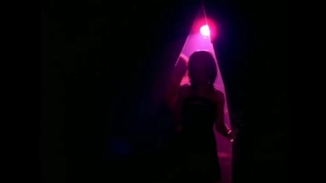 A still from Rihanna's "Don't Stop the Music" music video, showing her walking through a triangular opening in black curtains with a purple stage light shining at the top of the triangle.