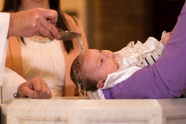 A priest pours water on a baby's head during a baptism ceremony.