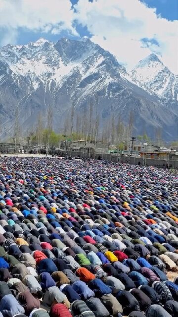 A large congregation of Muslims bowing in prayer during Jam'atul-Wida, the last Friday of Ramadan, in Skardu, Pakistan, with snow-capped mountains in the background.