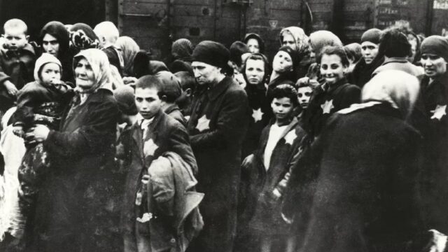 A group of Jewish people, including women and children, wearing yellow Star of David patches on their clothing, being forcibly relocated during the Holocaust.