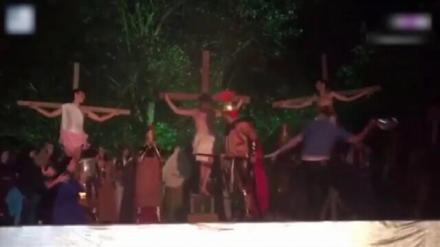 A scene from a Passion Play, depicting three individuals crucified on crosses with a Roman centurion standing nearby. A man can be seen attacking the centurion with a helmet.