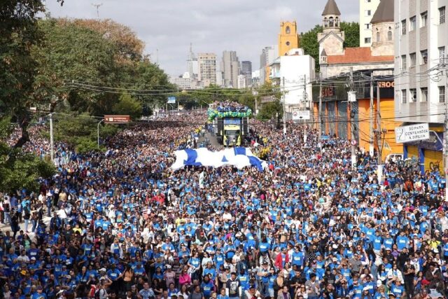 A large crowd of people participating in the "March for Jesus" event in Brazil, 2019. The participants, many of whom are wearing blue shirts, fill the streets as they march together in a demonstration of their faith.