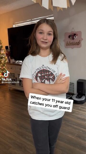 A young girl stands skeptical with her arms crossed, wearing a white T-shirt, in a home decorated for Christmas. The TikTok overlay reads, "When your 11 year old catches you off guard."