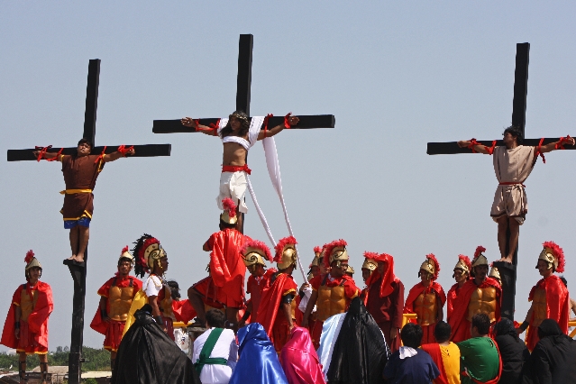 A reenactment of the crucifixion during Holy Week in the Philippines, featuring participants dressed as Roman soldiers and three individuals nailed to crosses as part of the traditional Penitensya rituals.