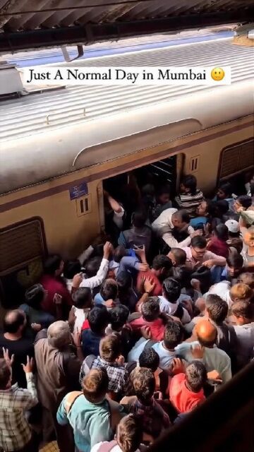 A crowded scene at a train station in Mumbai, with a large number of people pushing and shoving to enter and exit a train. The caption reads, "Just A Normal Day in Mumbai." The platform and train are packed with commuters, reflecting the busy and chaotic nature of daily life in the city.