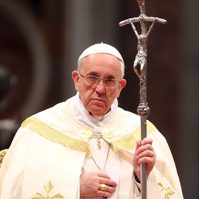 Pope Francis holding the Papal Ferula, a silver pastoral staff with a crucifix, during a religious ceremony. He is dressed in white papal vestments, with a solemn expression, and the background suggests a church setting.