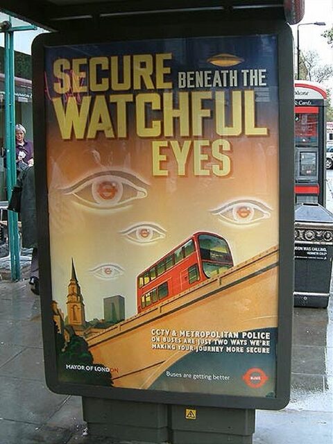 A bus stop poster in London promoting the use of CCTV on buses. The poster features large, stylized eyes watching over a red double-decker bus on an inclined road. The text reads, "Secure beneath the watchful eyes," highlighting the increased security measures.