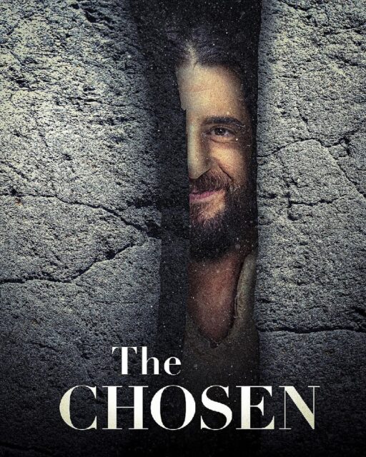 A promotional poster for the TV show "The Chosen" features a close-up of Jesus' face, partially revealed through a narrow crack in a stone wall. The left side of his face is visible, showing a sly smile. The texture of the stone surrounding the crack is rugged and dark. The title "The Chosen" is displayed prominently at the bottom in large white letters.