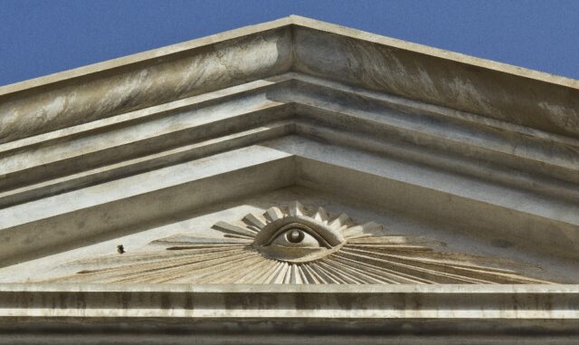 The Eye of Providence depicted on the exterior of the Masonic Temple in Santa Cruz de Tenerife, Spain. The eye is sculpted within a triangular pediment, with rays of light extending outward, set against the marble facade of the temple.