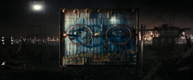 A billboard from "The Great Gatsby" (2013) featuring the large, bespectacled eyes of Doctor T. J. Eckleburg. The faded sign looms over a dark, industrial landscape, with city lights glowing faintly in the background. The billboard is weathered, suggesting neglect and decay, while the eyes seem to watch over the scene, symbolizing a sense of omniscient observation.