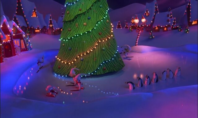 Children are skating around a massive decorated Christmas tree in the center of a snowy town square. The tree is adorned with colorful Christmas lights and ornaments. In the background, brightly lit houses and lamp posts contribute to the festive atmosphere, while a line of penguins watches the children skate.