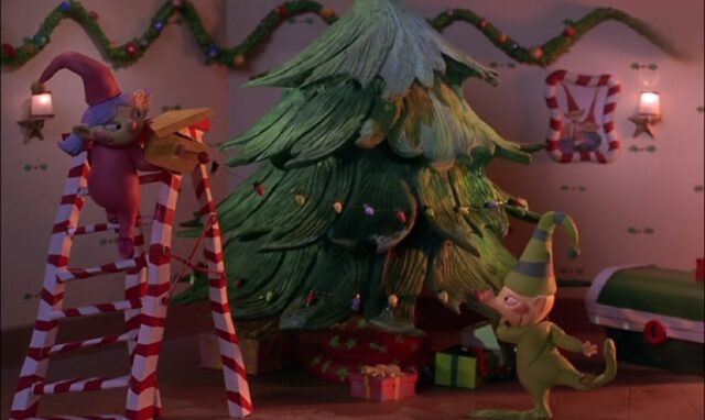 Two children wearing pajamas and Santa hats are decorating a Christmas tree. One child is spinning the Christmas tree while the other is decorating it from the top of a candy cane-striped ladder. The room is adorned with festive garlands, and presents are placed under the tree.