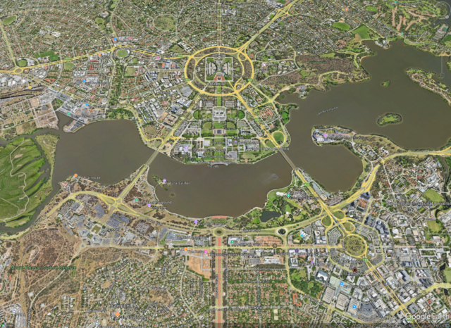 Aerial view of Canberra, Australia, showing the Parliamentary Triangle with key landmarks such as Parliament House, Old Parliament House, and Lake Burley Griffin, surrounded by structured roadways and green spaces.