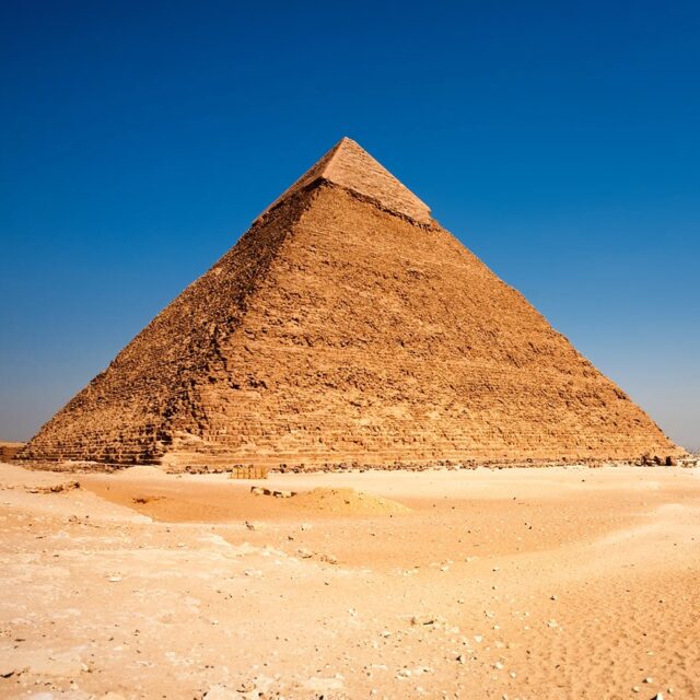 The Pyramid of Khafre in Giza, Egypt, with part of its original smooth limestone casing still visible at the top, set against a clear blue sky.