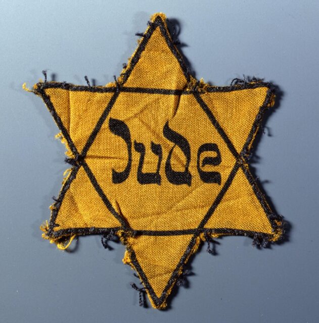 A worn yellow Star of David patch with the word "Jude" in the center, used by Nazis to identify Jews during the Holocaust.